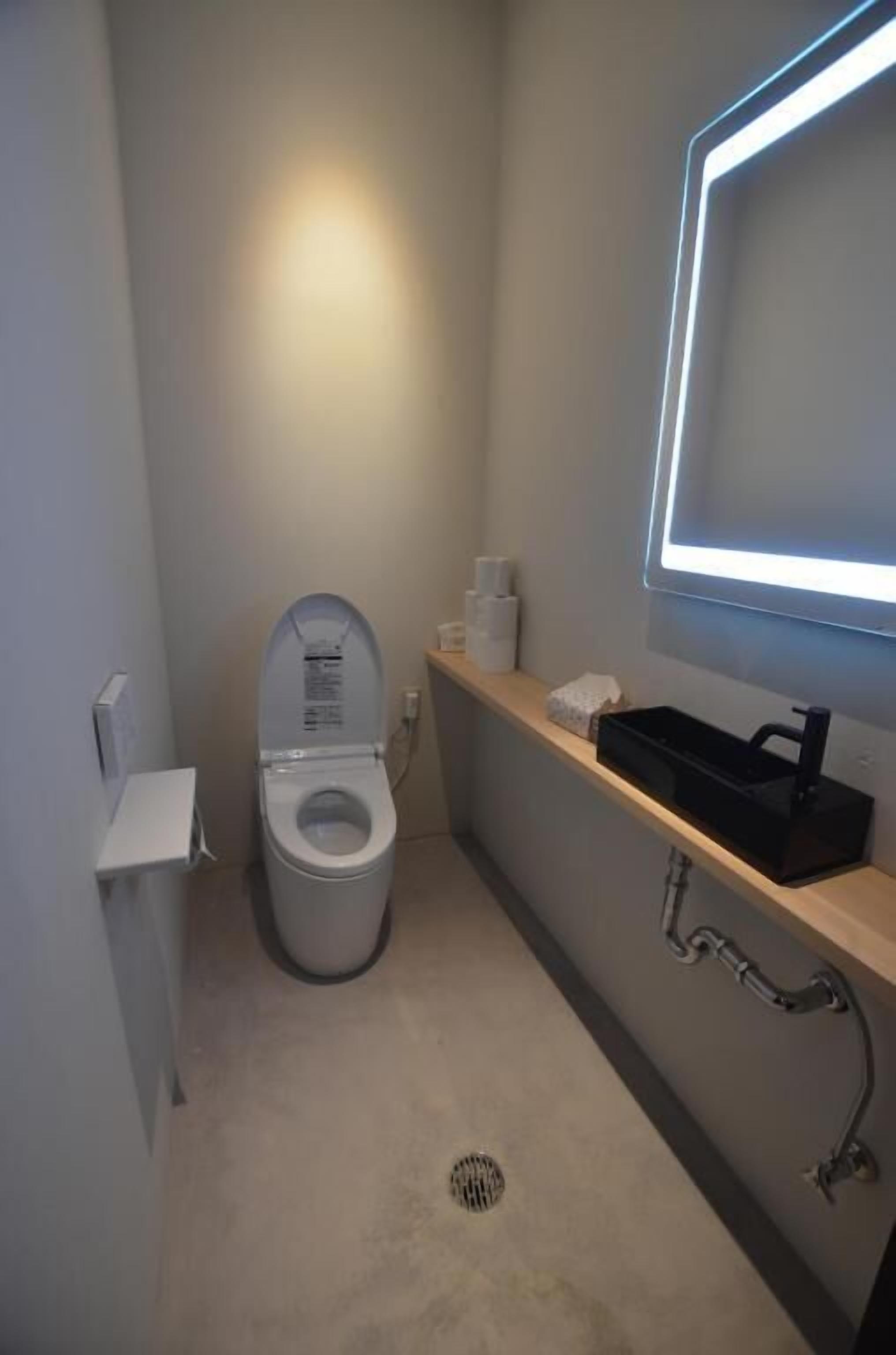 A compact bathroom with a toilet, a shelf with toiletries, and a wall-mounted mirror.