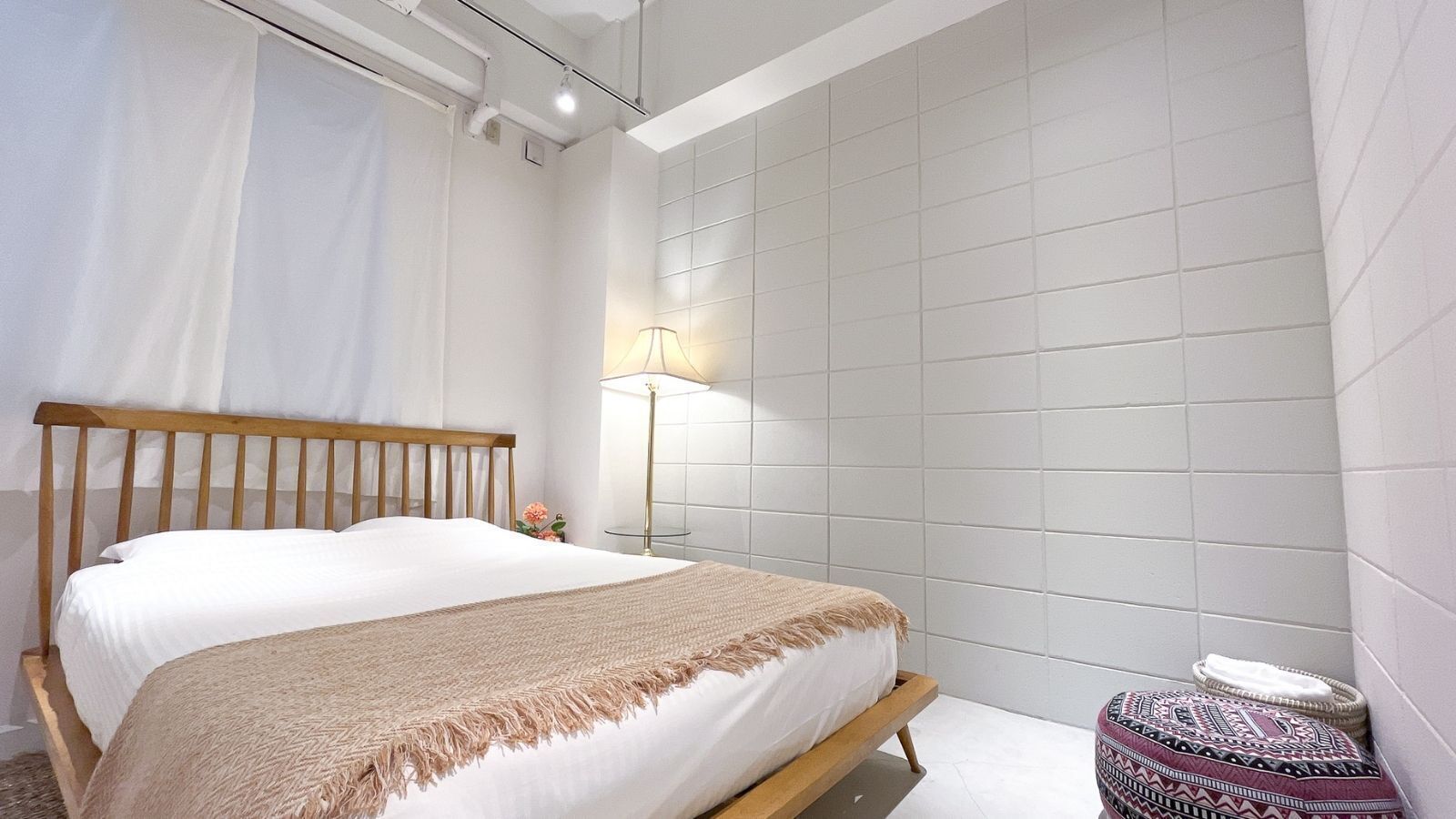 A bedroom with a bed, a bedside lamp, and a small round ottoman.