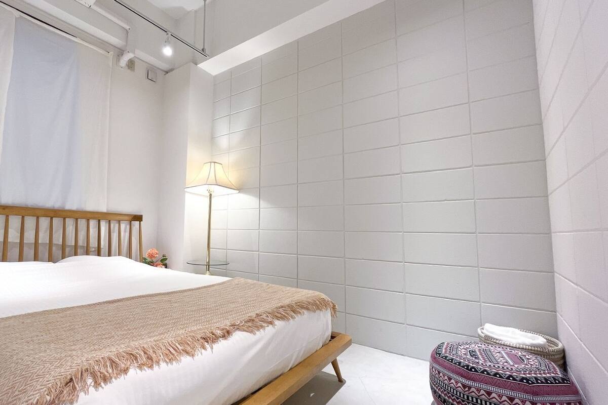 A bedroom with a bed, a bedside lamp, and a small round ottoman.