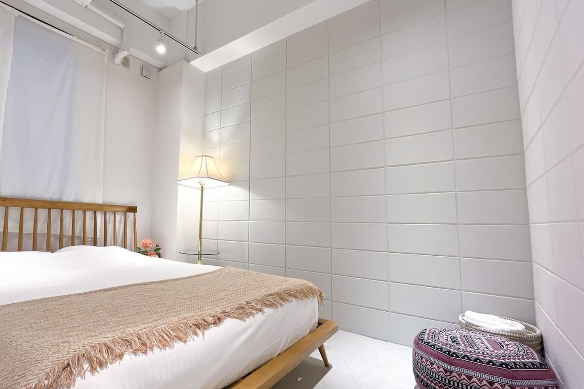 Un dormitorio con una cama, una lámpara de noche y un taburete redondo pequeño.