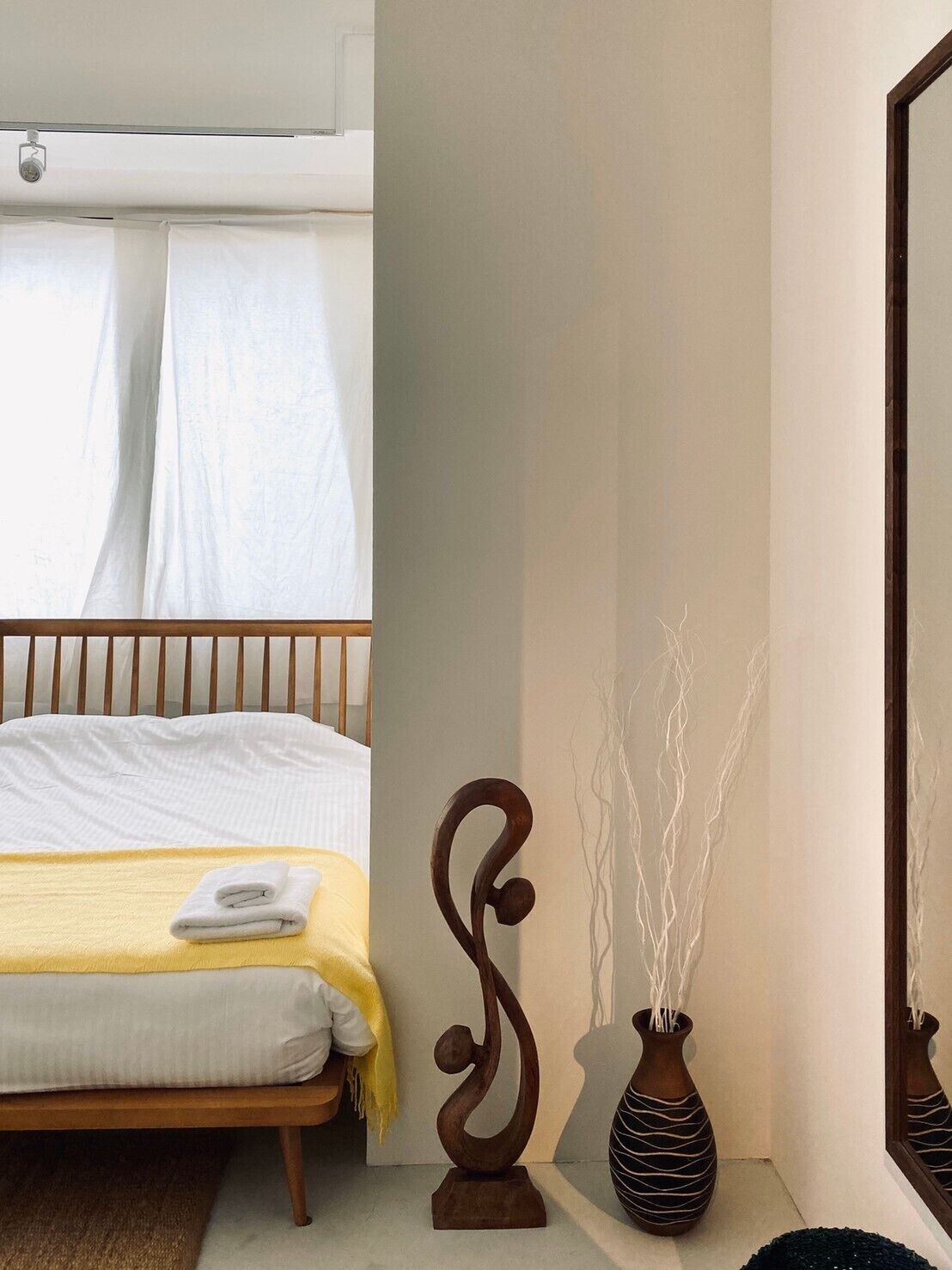 A bedroom with a bed, a wooden headboard, a bedside table with a vase, and a mirror on the wall.