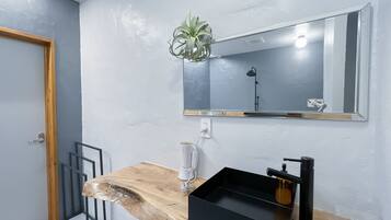 Un baño moderno con tocador de madera, lavabo negro y espejo.