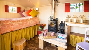 A cozy room with a bed, a wooden table with books and a tray, a wood-burning stove, and a window with red shutters. - Samsara Retreat and Yoga - Adults Only (Maidstone)