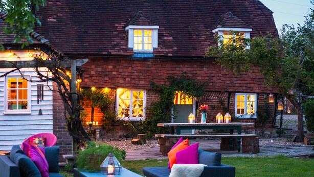 A cozy outdoor seating area with a bench and chairs, surrounded by a brick house with multiple windows and string lights. - Samsara Retreat and Yoga - Adults Only (Maidstone)