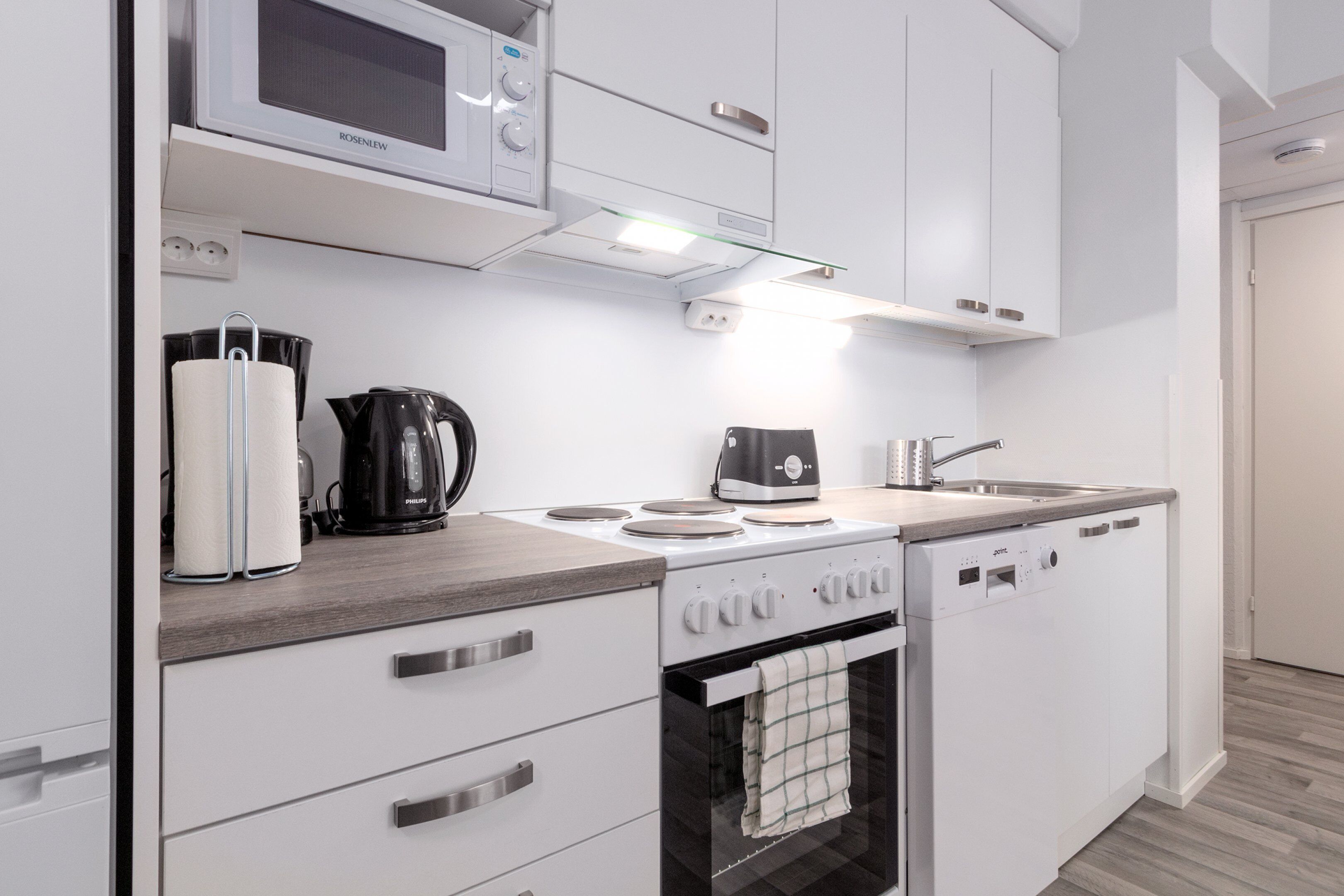 Una cocina moderna con armarios blancos, microondas integrado, cafetera y lavavajillas.