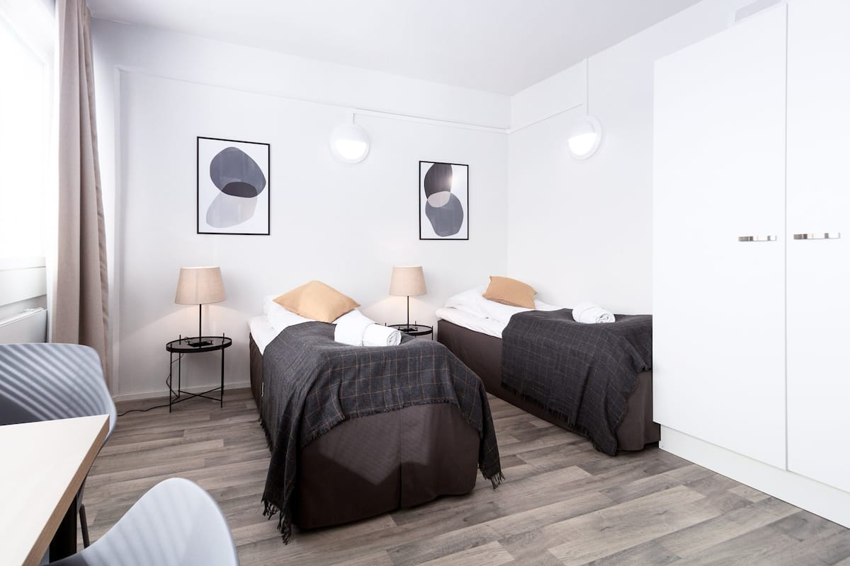 A modern hotel room with two beds, a desk, and a wardrobe.
