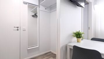 A modern, minimalist room with a white wardrobe, a mirror, a small table with a potted plant, and a black chair.