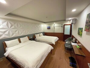 A hotel room with two beds, a wooden floor, a wall-mounted heater, a small table with a chair, and a door with a frosted glass panel. - Flaco Hostel Sapa (Sa Pa)