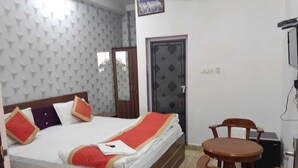 A hotel room with a bed, a small table and chairs, a wardrobe, and a door. - Hotel Shalimar Palace (Raebareli)