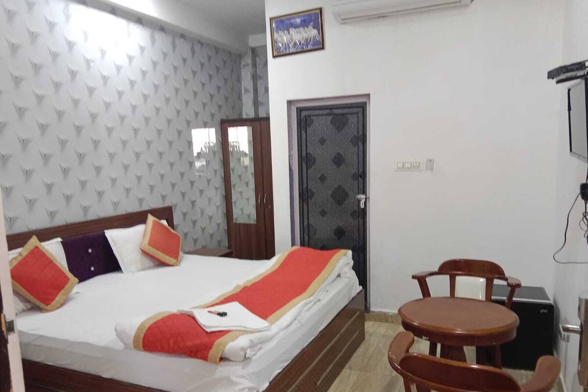 A hotel room with a bed, a small table and chairs, a wardrobe, and a door.