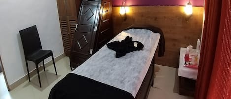 A small, neatly arranged bedroom with a bed, a chair, a wardrobe, and a bedside table with a lamp.