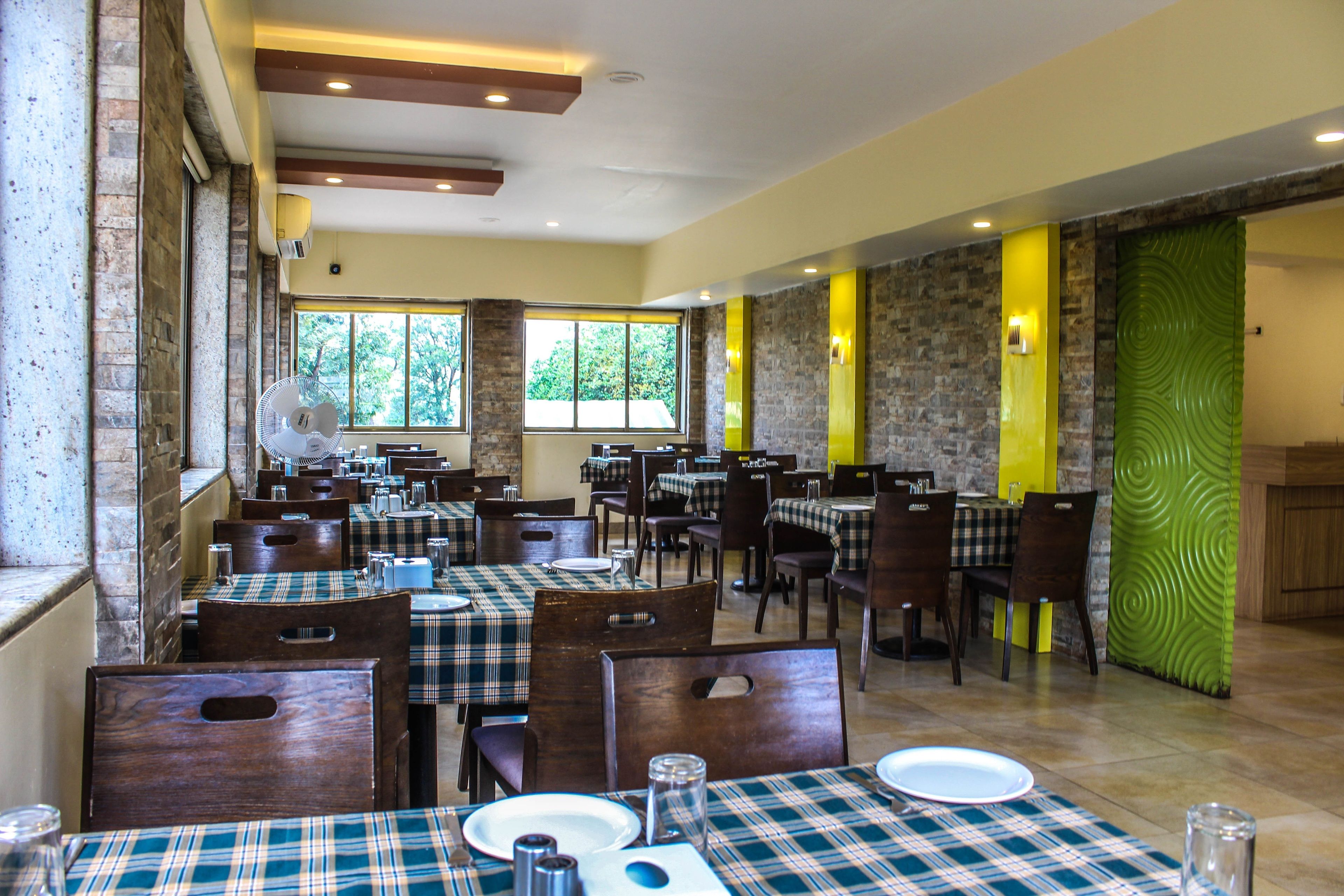 A restaurant with multiple tables and chairs, large windows, and a mix of brick and stone walls.