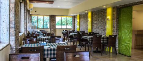 A restaurant with multiple tables and chairs, large windows, and a mix of brick and stone walls.