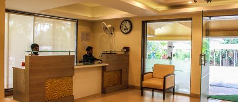 A reception area with a reception desk, two chairs, a clock, and a fan.