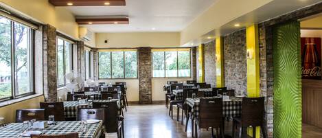 A spacious restaurant with multiple tables and chairs, large windows, and a stone wall with a Coca-Cola sign.