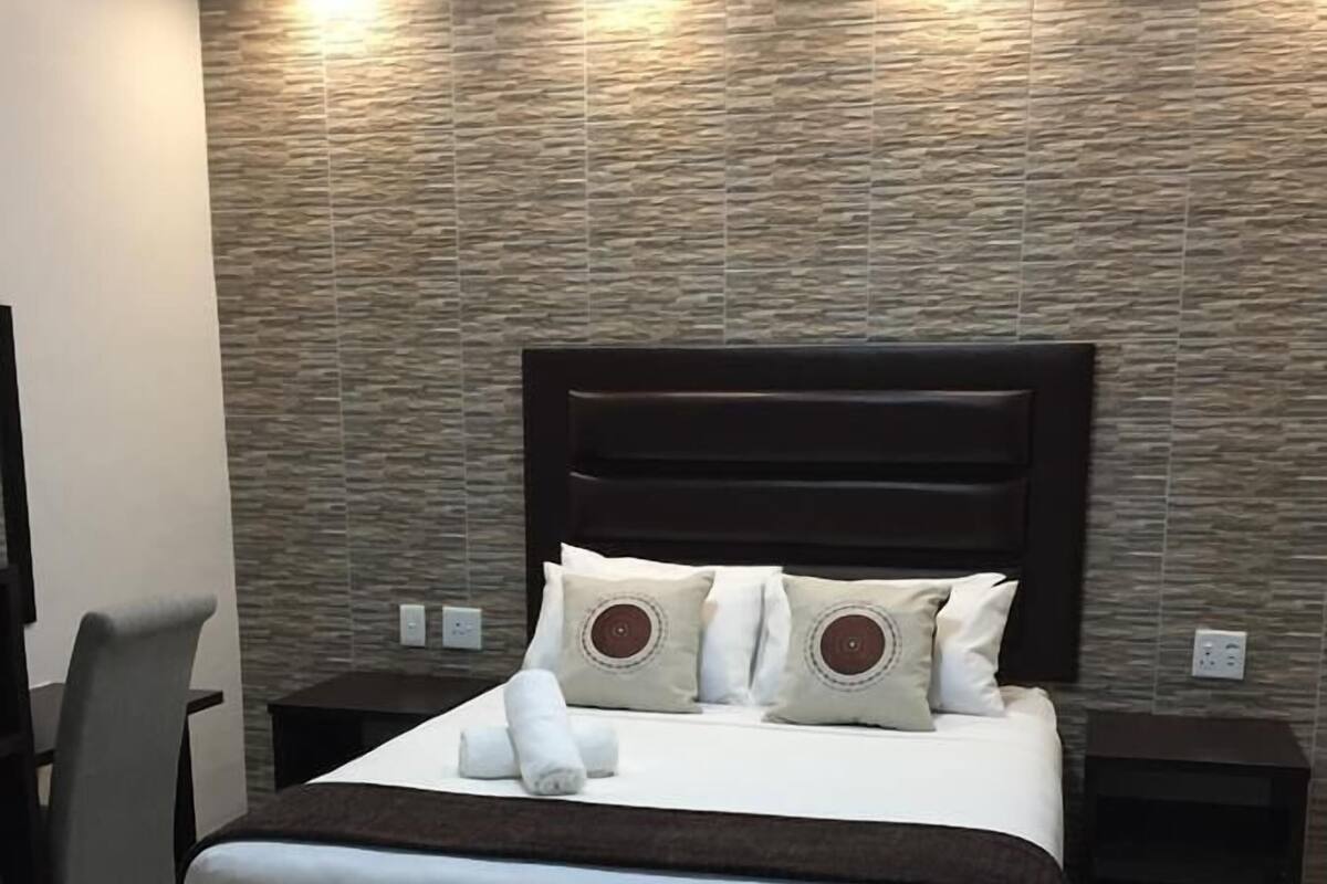 A modern bedroom with a large bed, two bedside tables, a chair, and a textured wall.
