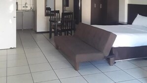 Una habitación con cama, un sofá marrón, una mesa de comedor con sillas, una zona de cocina y un armario de color oscuro.