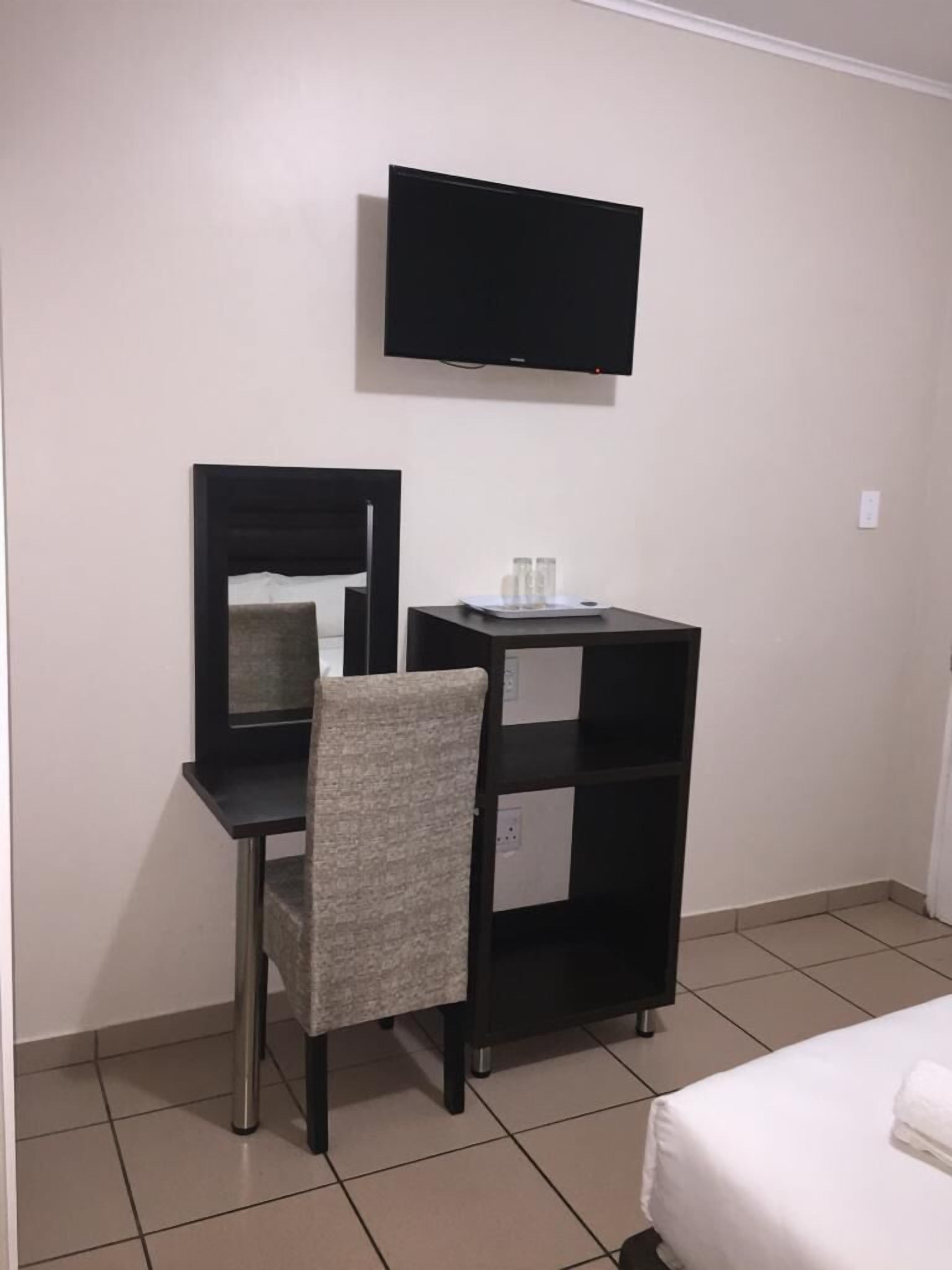 A hotel room with a desk, chair, TV, and a bed.