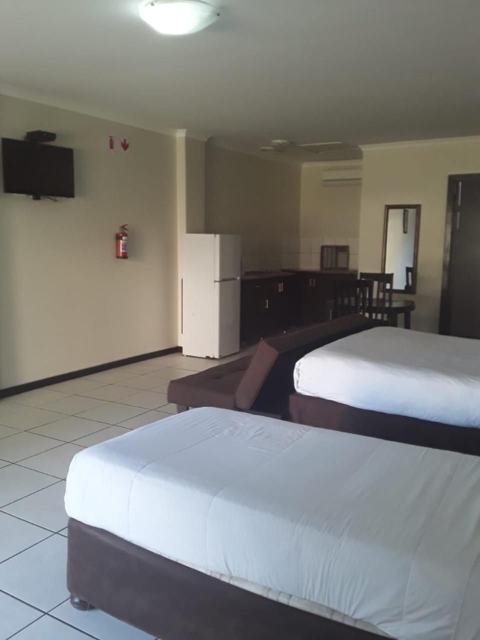 A hotel room with two beds, a kitchenette, a television, and a fire extinguisher.