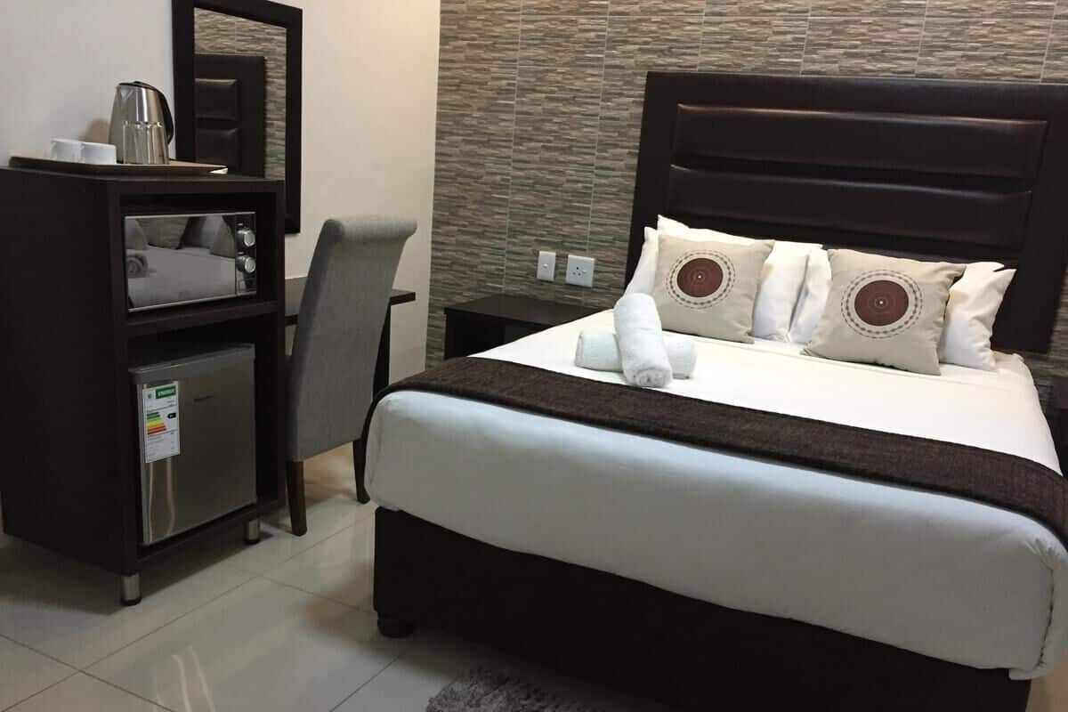 A hotel room with a bed, a desk with a coffee maker, and a small refrigerator.