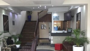 Un vestíbulo moderno con escaleras, zona de estar, mostrador de recepción y plantas en macetas.