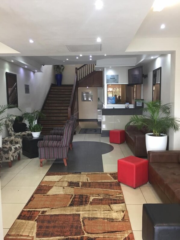 A modern lobby with a staircase, seating area, reception desk, and potted plants.