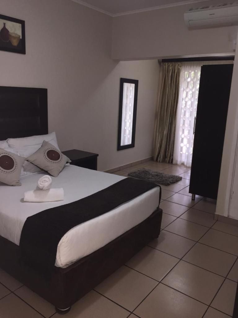 A hotel room with a bed, a nightstand, a window with curtains, and a door leading to another room.