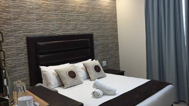 Una habitación de hotel moderna con una pared de textura pétrea, un cabecero oscuro y una cama bien hecha con dos almohadas.