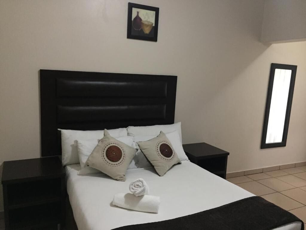 Een keurig opgemaakt bed met witte lakens en decoratieve kussens, een zwart hoofdbord en een klein nachtkastje.