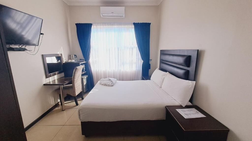 Une chambre d’hôtel avec un lit, un bureau et une chaise, une télévision et une fenêtre avec des rideaux.