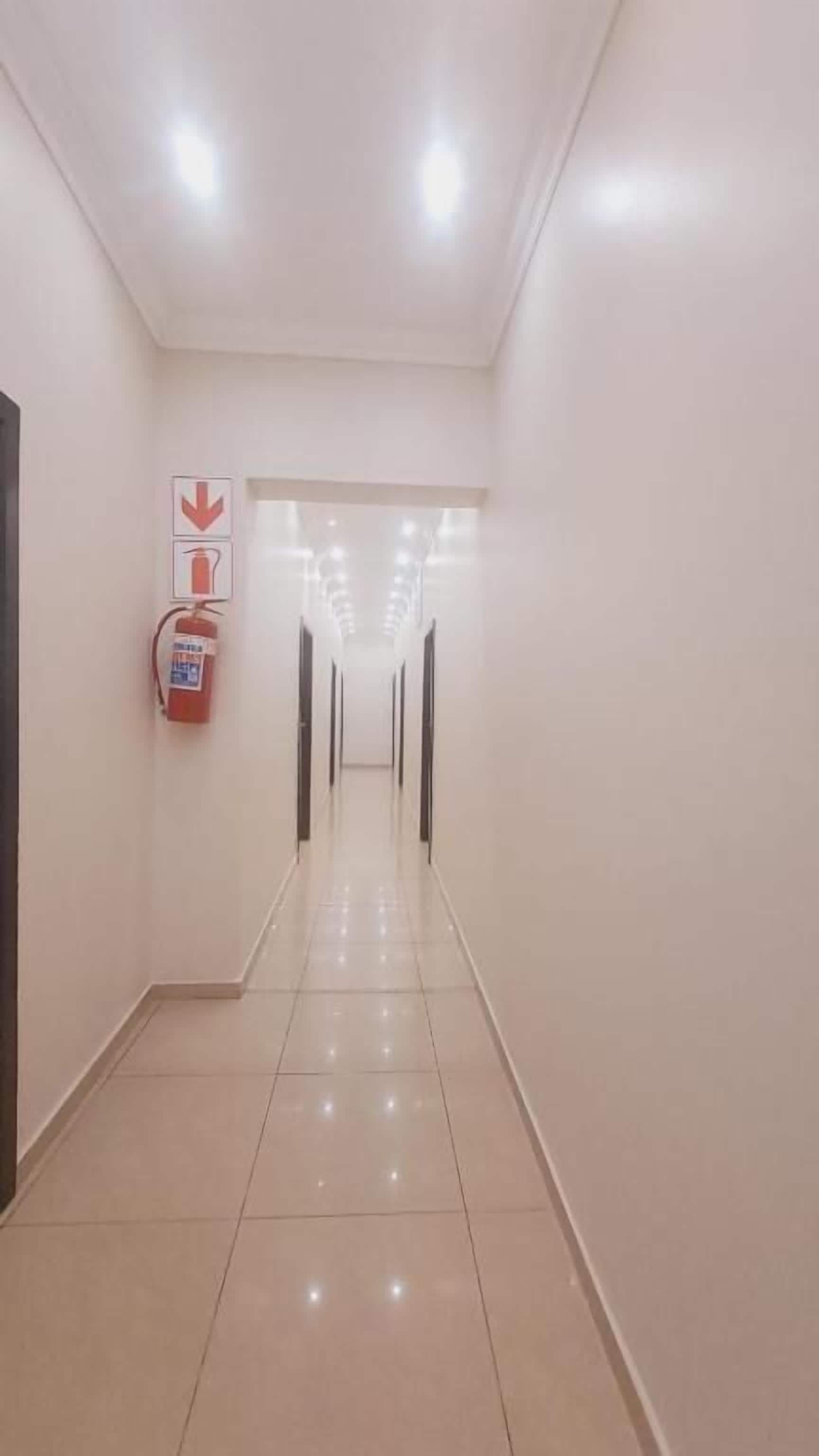 A long, well-lit corridor with a fire extinguisher on the left and a door at the end.