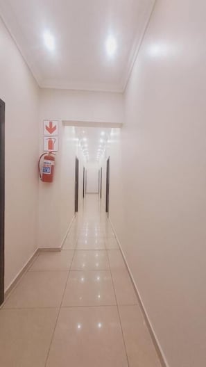 A long, well-lit corridor with a fire extinguisher on the left and a door at the end.