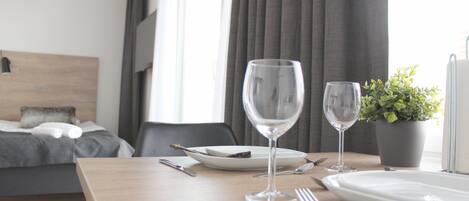 A neatly arranged dining table with a plate, two wine glasses, cutlery, and a potted plant in a modern hotel room.