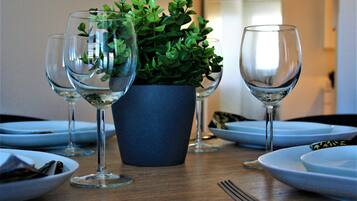 A dining table set with plates, cutlery, and wine glasses, with a potted plant in the center.