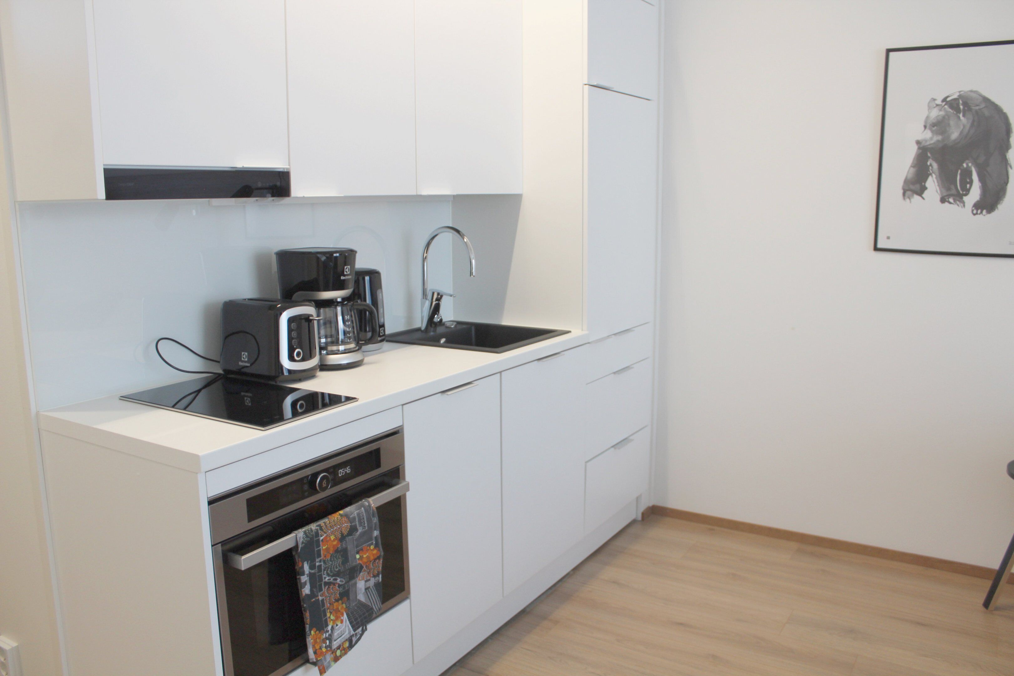 Una cocina moderna con armarios blancos, horno empotrado, cafetera y lavamanos.