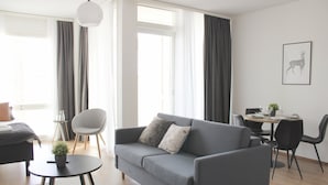 A modern living room with a grey sofa, a small round table with a plant, and a dining area with a table set for two. - Forenom Serviced Apartments Rovaniemi (Rovaniemi)