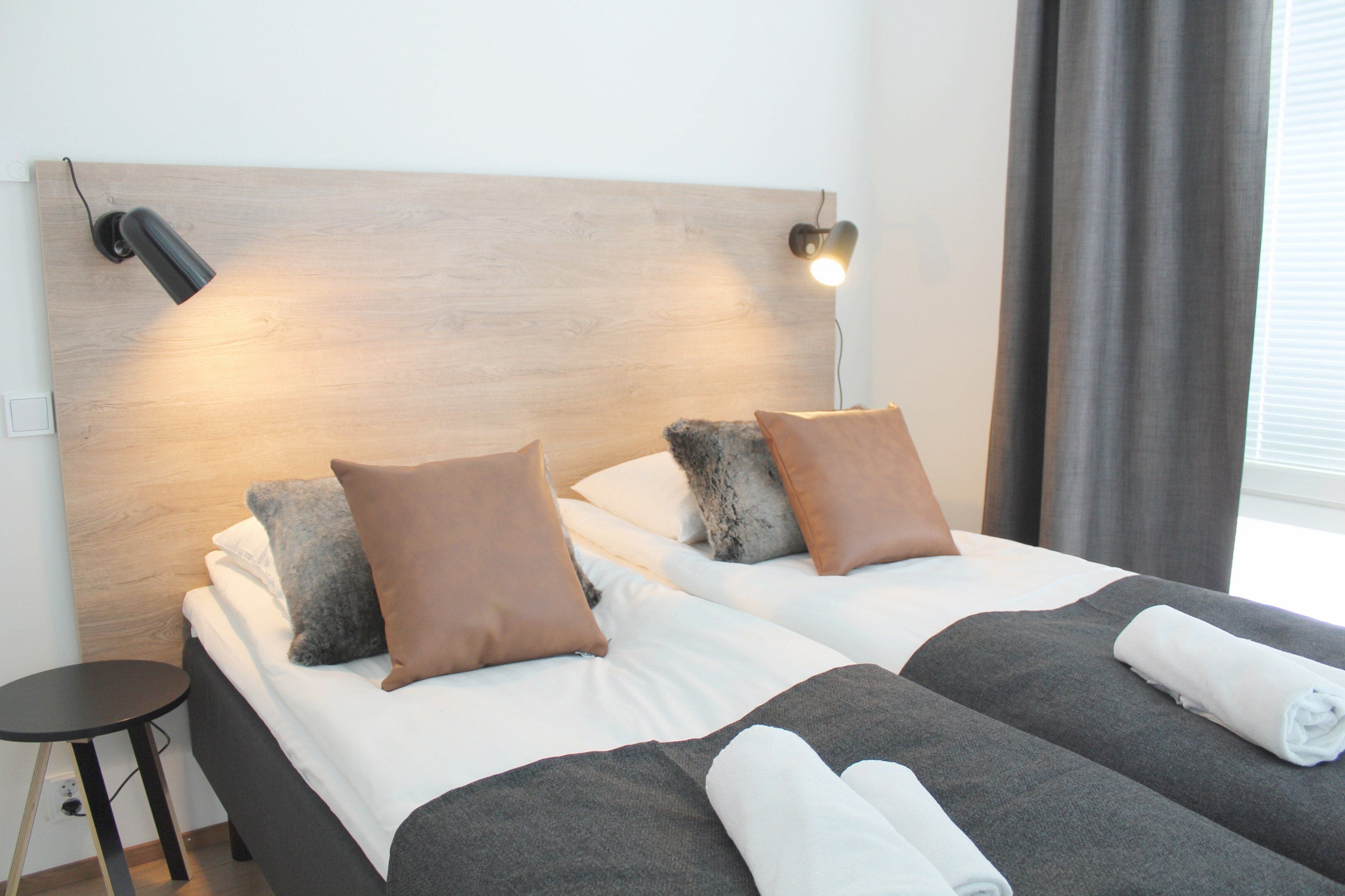 Habitación de hotel con dos camas, cada una con una manta gris y almohadas marrones, un cabecero de madera y una mesita de noche al lado de las camas.