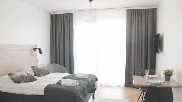 A modern hotel room with a bed, bedside table, and a desk with a chair. - Forenom Serviced Apartments Rovaniemi (Rovaniemi)