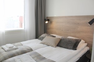 Una cama bien hecha con cabecera, lámpara de noche y ventana con cortinas.
