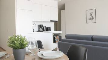 Un comedor con una mesa preparada para dos, una planta en maceta y un sofá gris.
