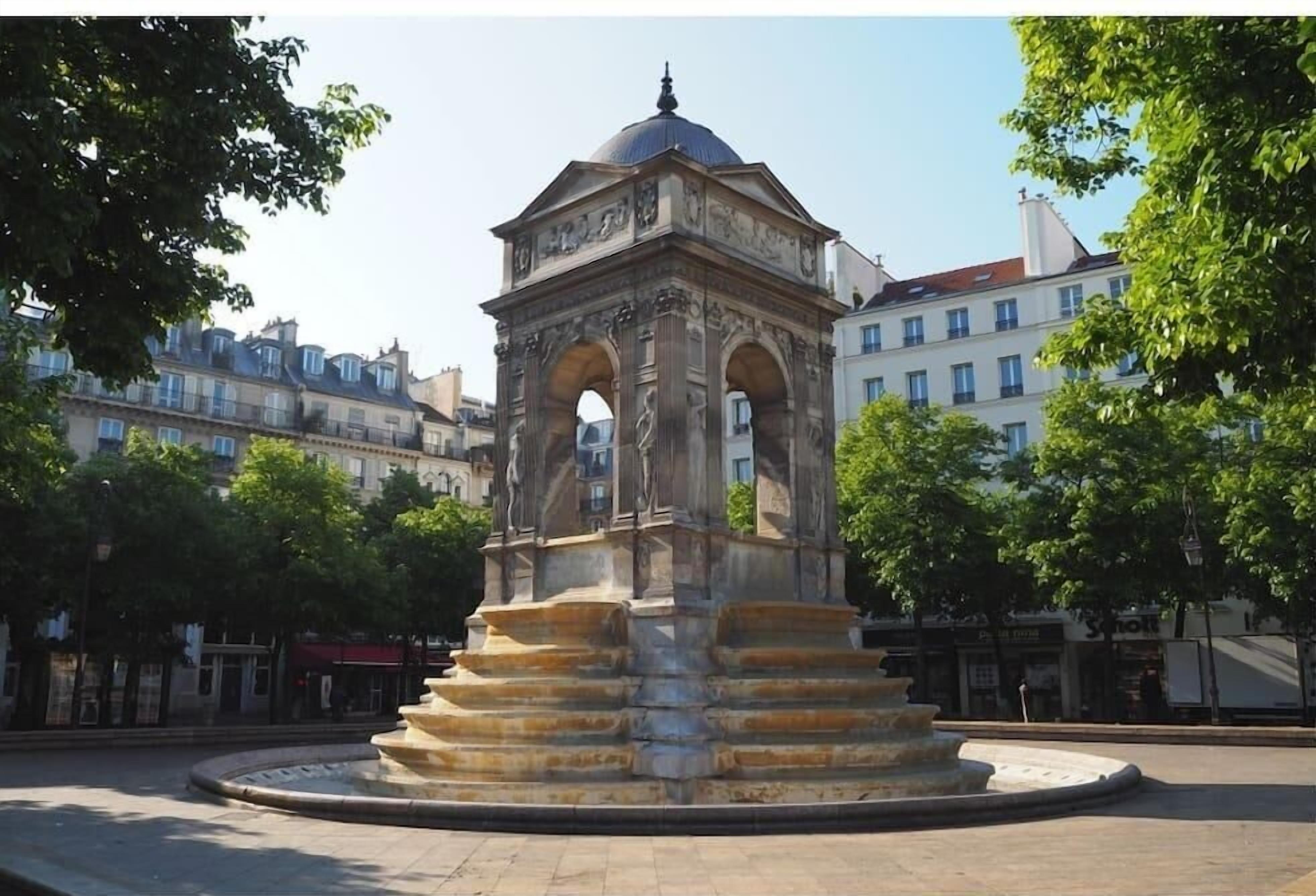 A stone monument with a dome and arches, surrounded by a circular plaza with trees.