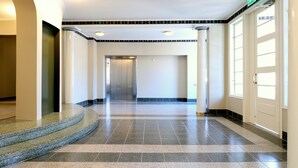 A clean, modern hallway with a curved staircase, a central elevator, and a door with an emergency exit sign. - Forenom Serviced apartmentsHelsinkiTöölö (Helsinki)