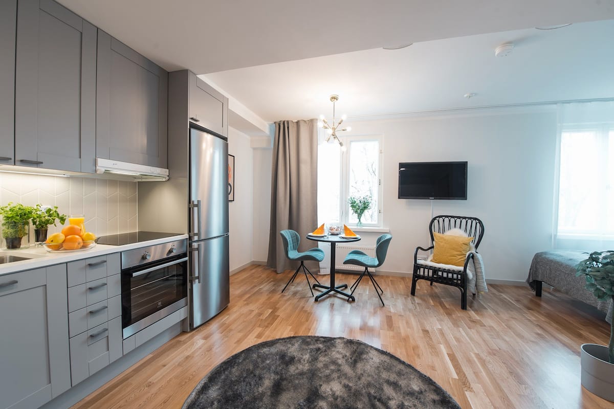 Une cuisine moderne avec des meubles gris, un four encastré et un coin repas comprenant une table et des chaises.