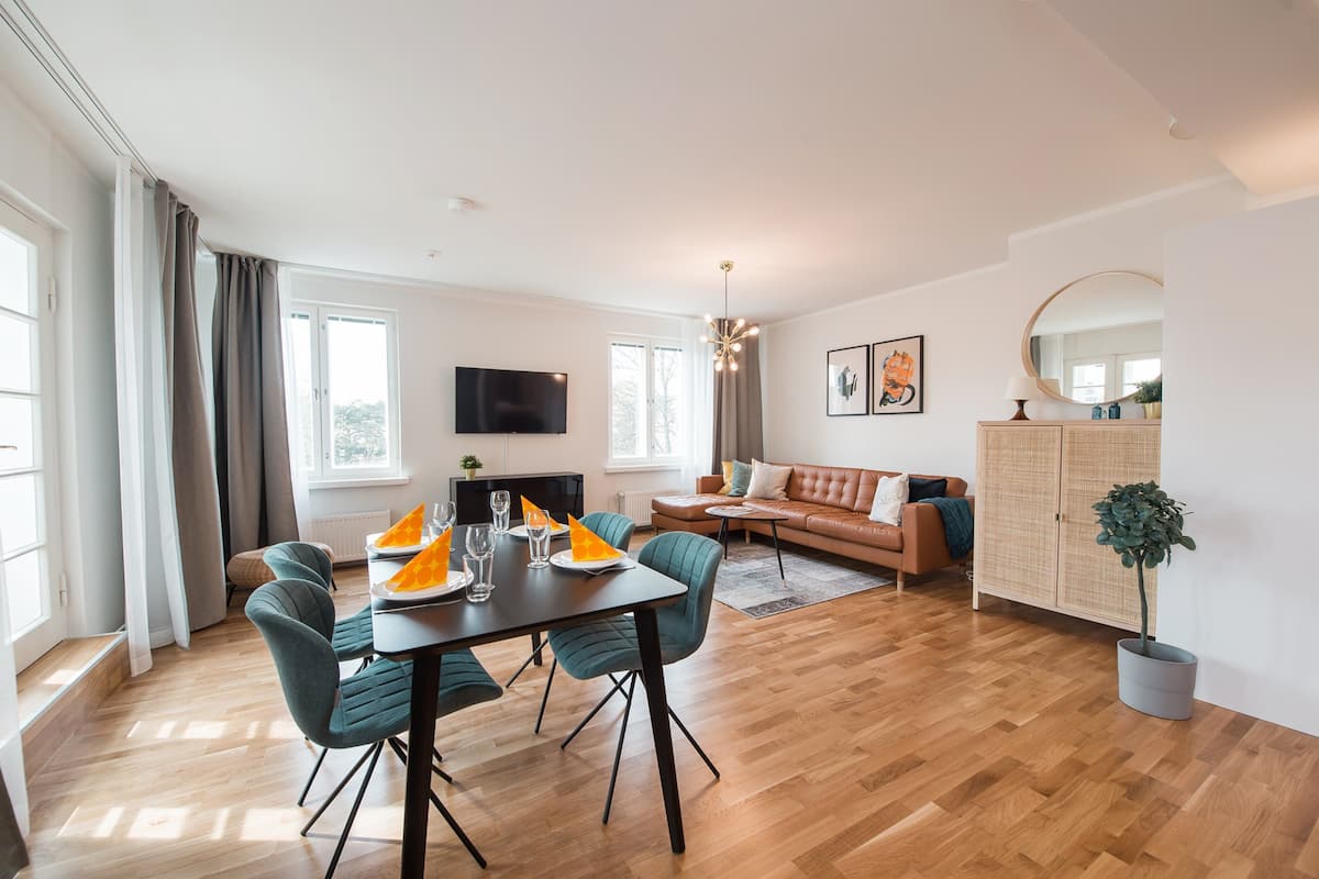 Un salon moderne comprenant un coin repas, un plancher en bois, un canapé, un téléviseur et une grande fenêtre.