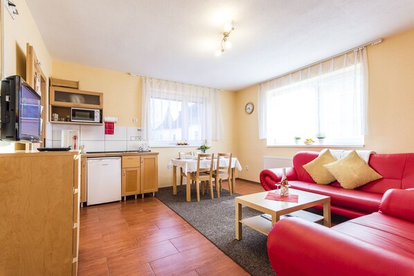 A compact living space with a kitchenette, dining area, and a red sofa. - Apartmány DREAMS (Besenova)