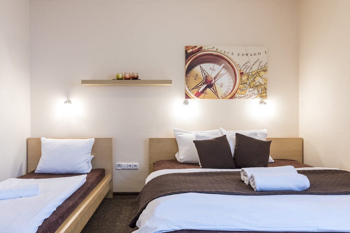 Habitación de hotel con dos camas, repisa de pared con objetos decorativos y un mapa de brújula grande en la pared.