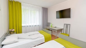 Habitación de hotel con dos camas, un escritorio, un televisor y un ventanal con cortinas.
