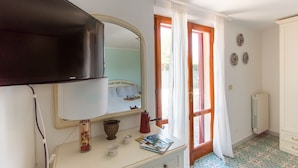 A bedroom with a bed, a TV, a dresser, and a window with curtains. - Villa Giolù (Portoferraio)