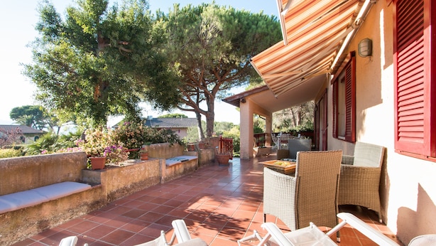A patio with outdoor furniture, a pergola, and a view of a tree and house in the background. - Villa Giolù (Portoferraio)