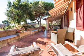 A patio with outdoor furniture, a pergola, and a view of a tree and house in the background. - Villa Giolù (Portoferraio)